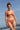 Une jeune femme debout sur la plage porte un bikini rose terracotta en seaqual.