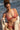 Jeune femme à la plage en bikini terracotta tient une fouta rayée rose et crème.