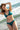Jeune femme portant un bikini vert émeraude en seaqual se tient dos à la mer.