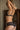 Femme blonde de dos, qui est en train de réajuster son soutien-gorge noir.