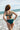 Jeune femme en bikini vert émeraude se tient face à la mer.
