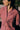 Close up of the Frances Unisex Cuban Shirt in red and white stripe. A woman is wearing the short sleeve shirt and the crop of the image shows the Saywood signature embroidered flower on the right chest pocket, and revere collar. Grass and a wooden fence can be seen behind her. She has her arms behind her back and is looking off to the side.