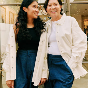 Mother & daughter wear matching white overshirts & blue adjustable waist jeans, smiling outdoors.