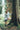 Woman in a forest leaning against a large tree in a Grey textured alpaca wool jumper