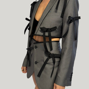 Model wearing upcycled grey with bows blazer set, transformed from a men's blazer into a cropped jacket and high waisted mini skirt.