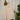 Saywood's Eddy Men's Colourblock Shirt in soft orange and pale yellow, with long sleeves, hangs on a copper hanger on a rope, in front of a white brick wall. Plants and dried flowers can be seen in the background.