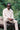 A black man sits on a log, surrounded by nature, with his hands clasped together in front of him. He wears Saywood's Eddy Mens Patchwork Shirt colourblocked in orange and pale yellow, with long sleeves. Worn with taupe chinos and sunglasses.
