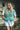 Woman wearing a green Mohair pointelle knit vest over a white shirt and light shorts, standing outdoors.