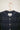 Close up of the Rosa Puff Sleeve Shirtdress in navy check, hanging on a hanger on a white wall. Only the neckline and shoulder gathers can be seen, with the Saywood label on the dress.