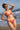 Jeune femme debout sur la plage en bikini terracotta regarde au loin, la main en visière.