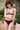 Une jeune femme dans un jardin porte un ensemble de lingerie couleur prune. 