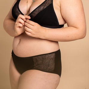 Jeune femme porte un ensemble de lingerie noir composé d'un soutien-gorge et d'un shorty en coton bio.