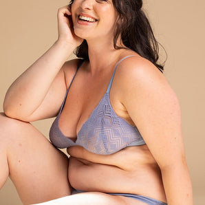 Jeune femme brune et souriante assise de face porte un soutien-gorge bleu clair.