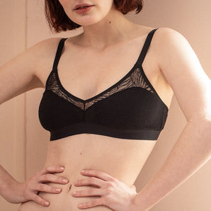 Une jeune femme se tient debout, les mains sur la taille et porte un ensemble de lingerie en coton biologique et dentelle recyclée. 
