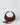 A dark brown suede crescent-shaped shoulder bag with gold-tone hardware, shown on a light gray studio background with its matching detachable strap placed in front.#color_chocolate-suede