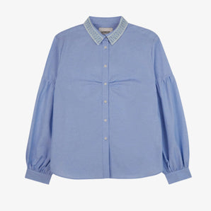 Womens pale blue shirt with lace trim collar and volume sleeves. Soft gathering is at the bust, with shirt made in recycled cotton. Shirt is on a white background