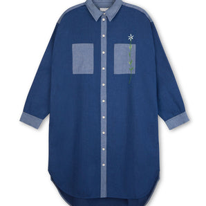 Womens Oversized Shirtdress in Japanese Denim, with lighter wash contrasting collar, placket, cuffs and pocket. Right pocket has a flower embroidery positioned through the pocket. Dress is on a white background.