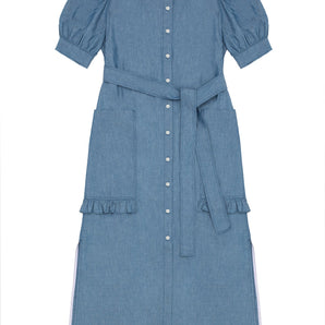 Womens denim puff sleeve dress in light wash Japanese denim, long line with side splits at the hem. Dress has patch pockets at the hip with ruffles at the bottom of the pockets, with a tied matching belt around the waist. Dress is on a white background.