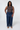 Woman in a fitted brown sleeveless top and adjustable waist jeans, posing with hands in pockets.