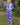 Woman wearing a blue and light blue patterned outfit standing in a garden.