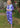 Woman wearing a blue and light blue patterned outfit standing in a garden.