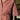 Close up of the Frances Unisex Cuban Shirt in red and white stripe. A woman is wearing the short sleeve shirt and the crop of the image shows the Saywood signature embroidered flower on the right chest pocket. Grass and a wooden fence can be seen behind her.