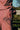 Close up detail shot of a woman wearing Saywood's Bessie A-line Shirts in berry red stripe. Shot from the back, the berry red cotton herringbone tape detail can be seen on the corner of the back patch pocket. The woman wears a matching shirt and is standing in front of a wooden fence with grass seen behind it.