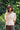A woman stands with her hands behind her back, surrounded by nature. She is wearing Saywood's Joni Puff Sleeve Blouse, with fit and flare darting, scallop hem adn lace trim on the collar. Worn with the Amelia Wide Leg Trousers in khaki cotton, and sunglasses.