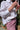 Close up of woman standing in front of a plant shop, wearing Saywood's Lela Boxy Shirt in white recycled cotton. The shirt is seen from the side, with the front tucked into the red berry stripe Bessie Short. She holds a pair of pink sunglasses in her hands.